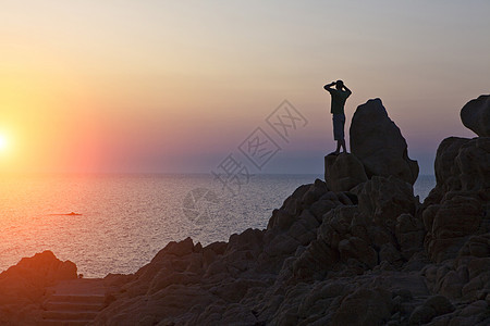意大利撒丁岛奥尔比亚岩石上的人在海上眺望日落的剪影图片