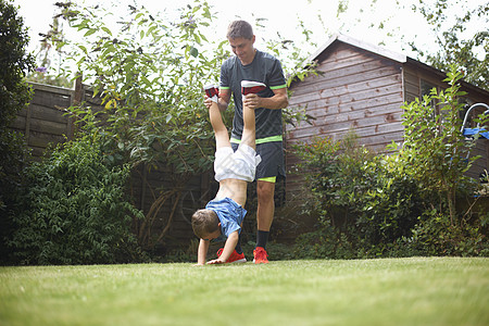 花园里父亲抬着儿子的腿帮他倒立图片