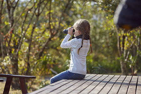木板上的孩子农村女孩坐在木板上透过望远镜看风景背景