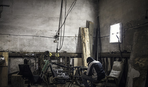 在用拆除的老式摩托车修配间用手扶椅坐着的机械师图片