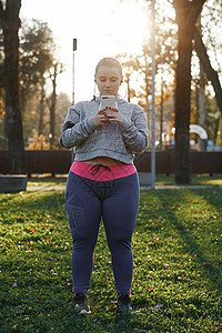 在公园中进行经济的年轻女子训练看智能手机图片