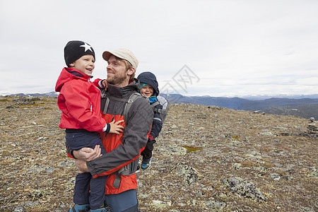 挪威奥普兰州洛美公园山地上背着一个孩子抱着一个孩子的男远足者图片