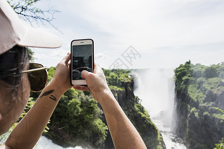 智能手机拍摄维多利亚瀑布照片的年轻女旅游青年图片
