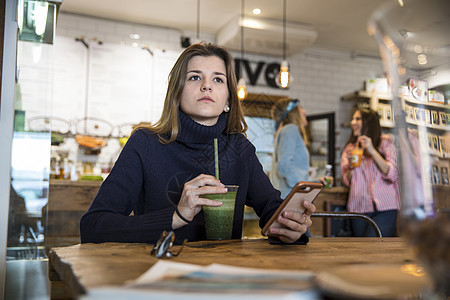 坐在咖啡馆的年轻女人拿着智能手机和饮料图片