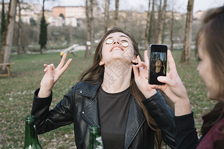 女人拍摄朋友在脸颊上平衡瓶盖的照片图片