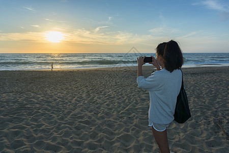 在海滩拍摄日落照片的女人图片