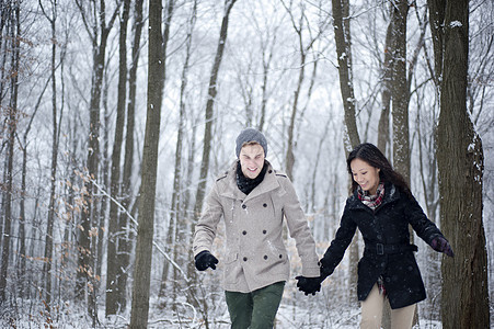 在加拿大安略省雪覆盖的森林中手牵行走的年轻夫妇图片