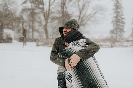 在雪地上用毯子包着妻子的男人图片