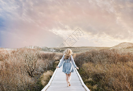 一名赤脚年轻女子在海岸沙丘木板路上散步图片