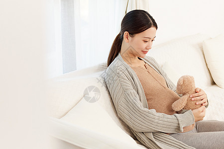 怀孕女性坐在沙发上抱着公仔背景图片
