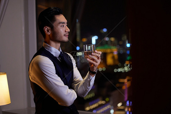 男性端着酒杯在欣赏夜景图片