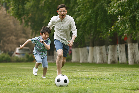 小孩动作快乐父子在草地上踢足球背景