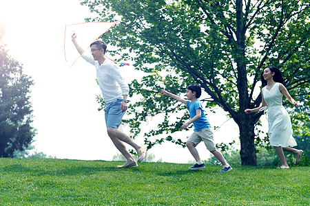 一家三口郊游高兴学龄前儿童成年人一家三口在草地上放风筝背景