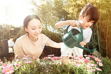 年轻妈妈年轻的母亲和女儿在浇花背景