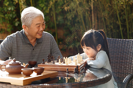 老人和小孩欢乐老年人象棋祖父和孙女在庭院里下棋背景