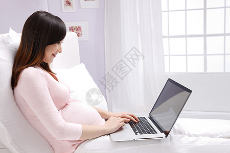 打字母亲东方人孕妇坐在床上看电脑图片