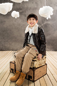 灰色风格小男孩坐在复古行李箱上背景