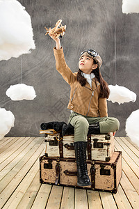 云上的飞机坐在行李箱上的女孩拿着飞机模型背景