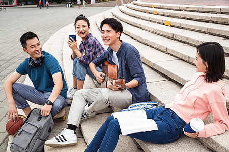 四个人不看镜头笑年轻的大学生坐在台阶上弹吉他图片