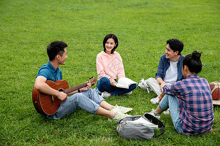 成人教育书包弹奏快乐的大学生在草地上弹吉他唱歌高清图片