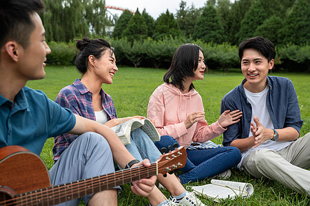 拿着欢乐草坪快乐的大学生在草地上弹吉他唱歌图片