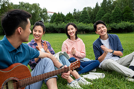 四个人弹奏课外活动快乐的大学生在草地上弹吉他唱歌高清图片