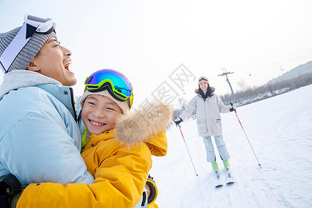 快乐滑雪场上抱在一起的父子和滑雪的母亲图片