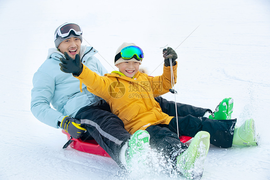 兴奋的父子坐着雪上滑板滑雪图片