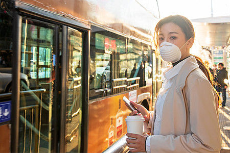 汽车车站防疫戴口罩的年轻女人站在公交车站背景