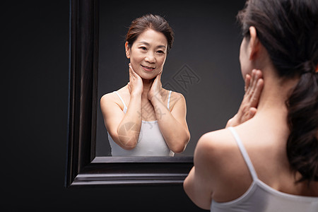 优雅的中年女人对着镜子做颈部护理高清图片