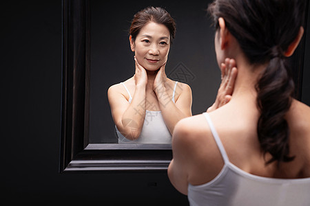 中年漂亮的中老年女对着镜子做颈部护理背景