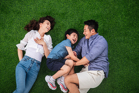 郊游亚洲8到9岁快乐的一家三口躺在草地上嬉戏背景