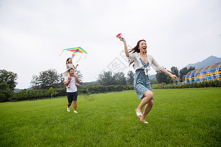 25岁到29岁郊区微笑快乐的一家三口在草地上放风筝图片