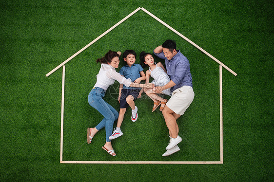 幸福的四口之家躺在草地上的房子轮廓里图片