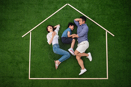 侧卧嬉戏的独生子女家庭快乐的一家三口躺在草地上的房子轮廓里玩耍图片