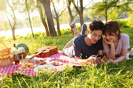 趴在草地上看手机的幸福情侣高清图片