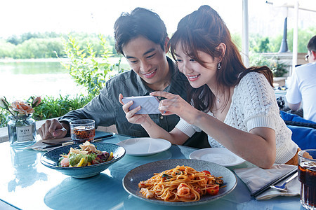 青年情侣在餐厅里用手机拍照图片