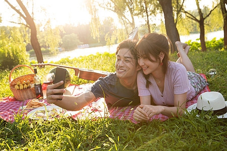 郊游活力欢乐趴在草地上拍照的幸福情侣图片