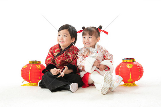 有趣的嬉戏的全身像兄妹两人穿新衣服坐在地上庆祝新年图片