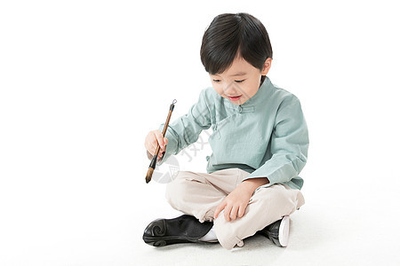 影棚拍摄传统节日节日可爱的小男孩坐在地上用毛笔写字图片