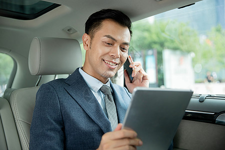 商务男士坐在汽车里拿着平板电脑打电话图片