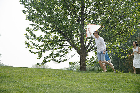 户外青年男人树一家三口在草地上奔跑图片