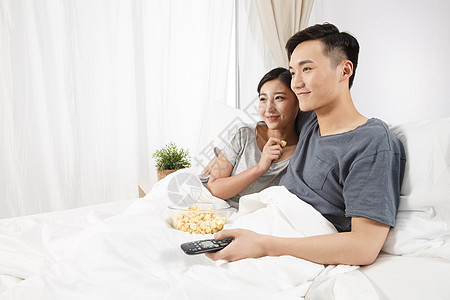 青年伴侣控制20多岁青年情侣坐着床上看电视背景图片