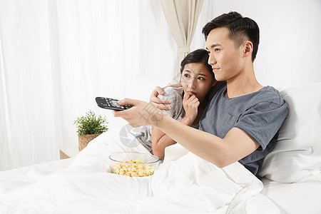 挨着时尚家庭生活青年情侣坐着床上看电视背景图片