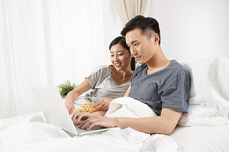 女朋友挨着起居室青年情侣坐着床上看电脑图片
