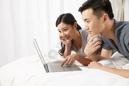 金色科技夫妇相伴笔记本电脑青年情侣趴在床上看电脑背景