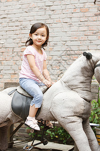 垂直构图户外活动玩具可爱的小女孩在骑摇摆木马图片素材