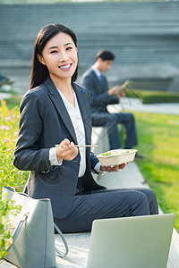 商务女士坐着户外边吃饭边工作高清图片