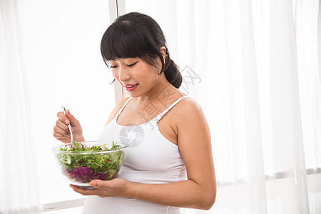 轻松母亲站着幸福的孕妇吃蔬菜沙拉图片