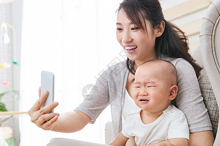 年轻妈妈和哭泣的宝宝用手机照相图片